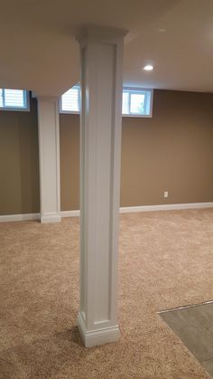 an empty room with carpeted floor and white pillars in the center, along with two windows