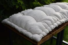 a bench cushion sitting on top of a wooden table next to some trees and grass