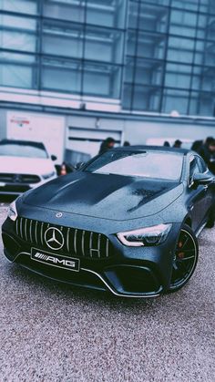 a black sports car is parked in front of a building with many other cars behind it