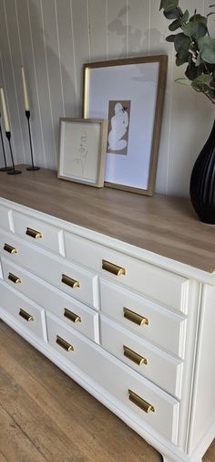 a white dresser with gold handles and drawers in a room next to a black vase