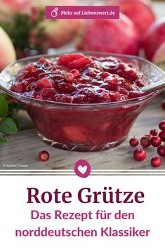 a bowl filled with cranberry sauce sitting on top of a table next to apples