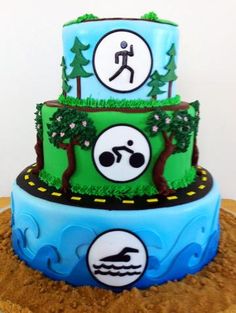 a three tiered cake decorated with green and blue icing, trees, and symbols