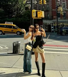 two women standing on the sidewalk taking pictures with their cell phones in front of a traffic light