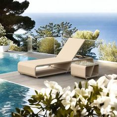 an outdoor lounge chair next to a swimming pool with the ocean in the back ground