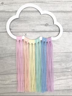 a rainbow fringe wall hanging with a cloud shaped decoration above it on a wooden background