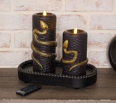 two candles with snakes on them are sitting on a tray next to a remote control