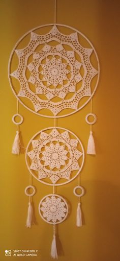 a white crocheted doily hanging on a yellow wall with tassels