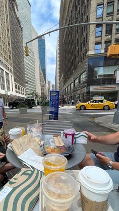 two people sitting at a table with food and drinks on it in the middle of a city