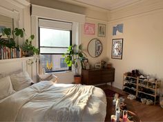 a bedroom with a bed, dresser and window in the corner that has plants on it