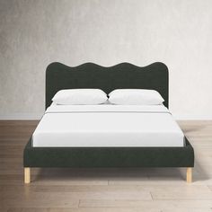 a bed with white pillows and green headboard on wooden flooring in front of a gray wall