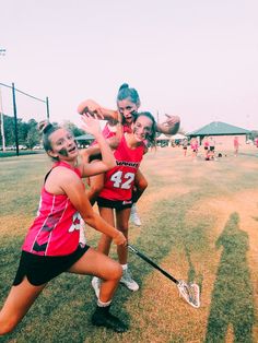 three girls in pink uniforms playing lacrosse on grass with one girl reaching for the ball