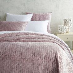 a bed with pink bedspread and pillows in a room next to a night stand