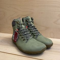 a pair of green hiking boots sitting on top of a wooden table next to a wall