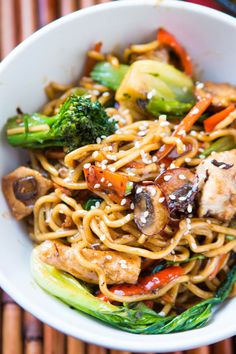 a white bowl filled with noodles and veggies on top of a wooden table