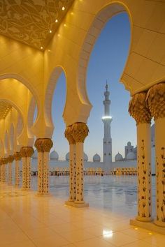 the inside of a building with columns and lights on it's sides, in front of a large body of water