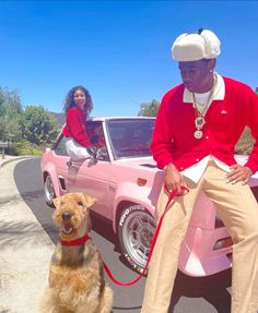 a man sitting on top of a pink car next to a brown dog