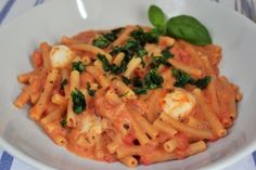 a white bowl filled with pasta covered in sauce and spinach garnished with cheese