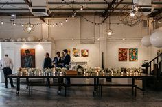 three men standing in front of a long table with candles on it and paintings hanging from the ceiling