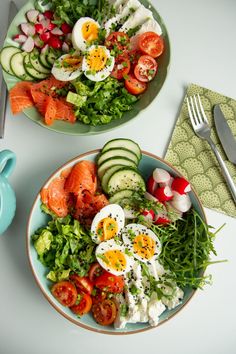 two plates filled with different types of food on top of a white table next to utensils