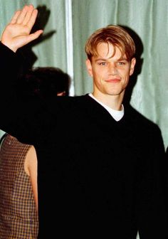 a young man waves to the camera while standing in front of a curtain