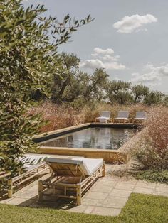 an outdoor swimming pool surrounded by trees and grass with two lounge chairs in the foreground