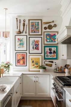 a kitchen with white cabinets and pictures on the wall above the stove, along with various utensils