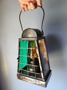 a hand holding an old fashioned lantern with two bottles in it's caged holder