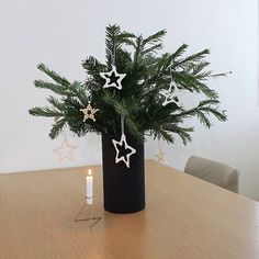 a christmas tree in a black vase with white stars on it and a lit candle