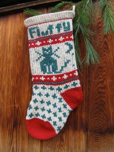 a knitted christmas stocking hanging on a wooden wall with pine needles and branches