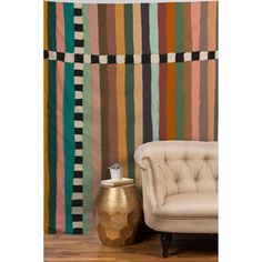 a chair sitting next to a wall covered in multicolored striped fabric and a gold vase