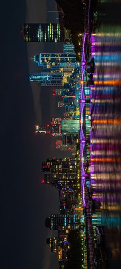 the city skyline is lit up at night with colorful lights and buildings in the background