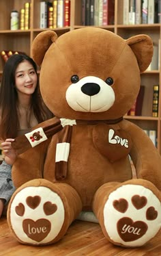 a woman sitting on the floor with a large teddy bear in front of bookshelves