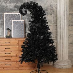 a black christmas tree on a stand in front of a wall