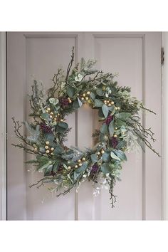 a wreath hanging on the front door with greenery, berries and pineconis