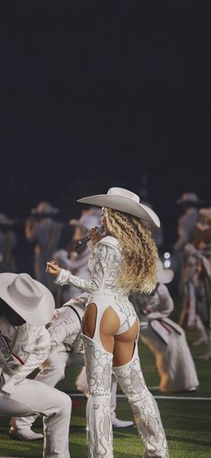 a woman in white outfit and cowboy hat standing on grass with other dancers behind her