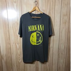 a black nirvana t - shirt hanging on a wooden wall next to a hanger