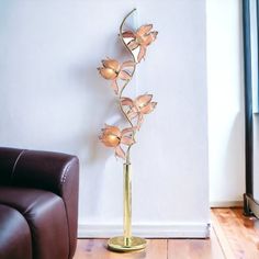 a gold vase with flowers in it sitting next to a brown leather chair and white wall