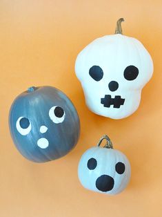 three painted pumpkins with faces on them sitting next to each other in front of an orange background