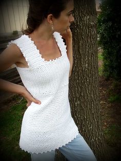 a woman standing next to a tree with her hands on her hips, wearing a white crocheted top