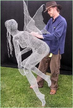 a man standing next to a wire sculpture on top of a green grass covered field