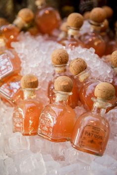 several small bottles are sitting on ice with corks in the top one is filled with orange liquid