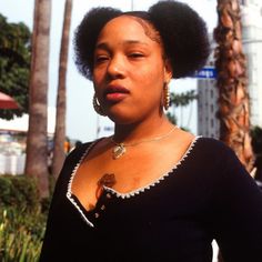 a woman with an afro standing in front of palm trees and looking off into the distance