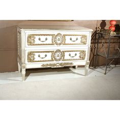 an antique white and gold painted chest of drawers in a room with other items on the floor