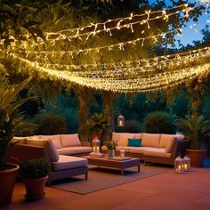 an outdoor living room is lit up with fairy lights and potted trees in the background