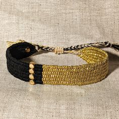 two black and gold beaded bracelets sitting on top of a white cloth covered surface