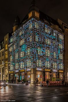 an illuminated building on the corner of a street at night with cars driving by it