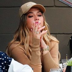 a woman sitting at a table with her hands in her mouth and wearing a hat