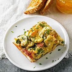 a white plate topped with slices of bread and veggie casserole next to a glass of orange juice