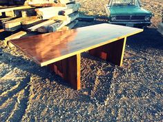 a wooden table sitting on top of a dirt field next to a green old car