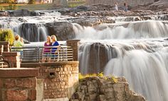 three people are standing on a bridge over a waterfall and looking at the falls below